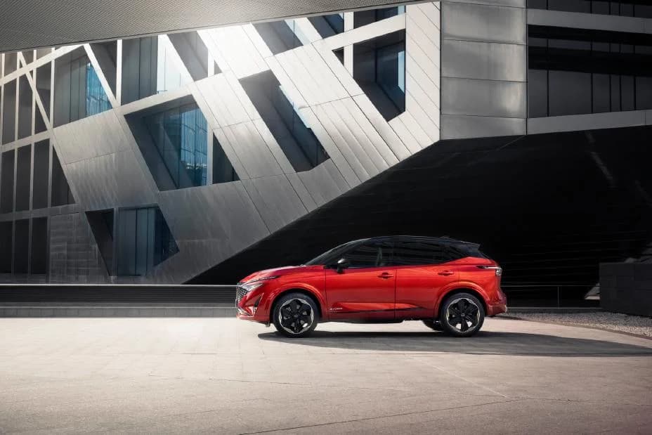 Red Nissan Qashqai parked beside a modern building, side view
